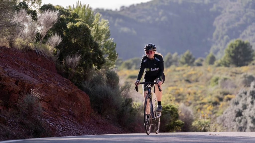 Woman cyclist riding a road bike uphill in a rural mountain landscape, showcasing endurance and sport.
